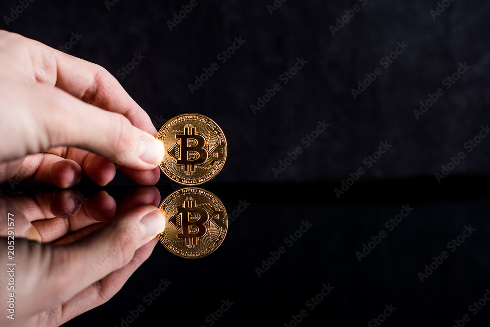 Fototapeta premium bitcoin in hand on a black background. Mirror reflection of a coin