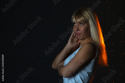 Girl in the white shirt and water drops behind and arround her illuminated by light during a photoshoot with water