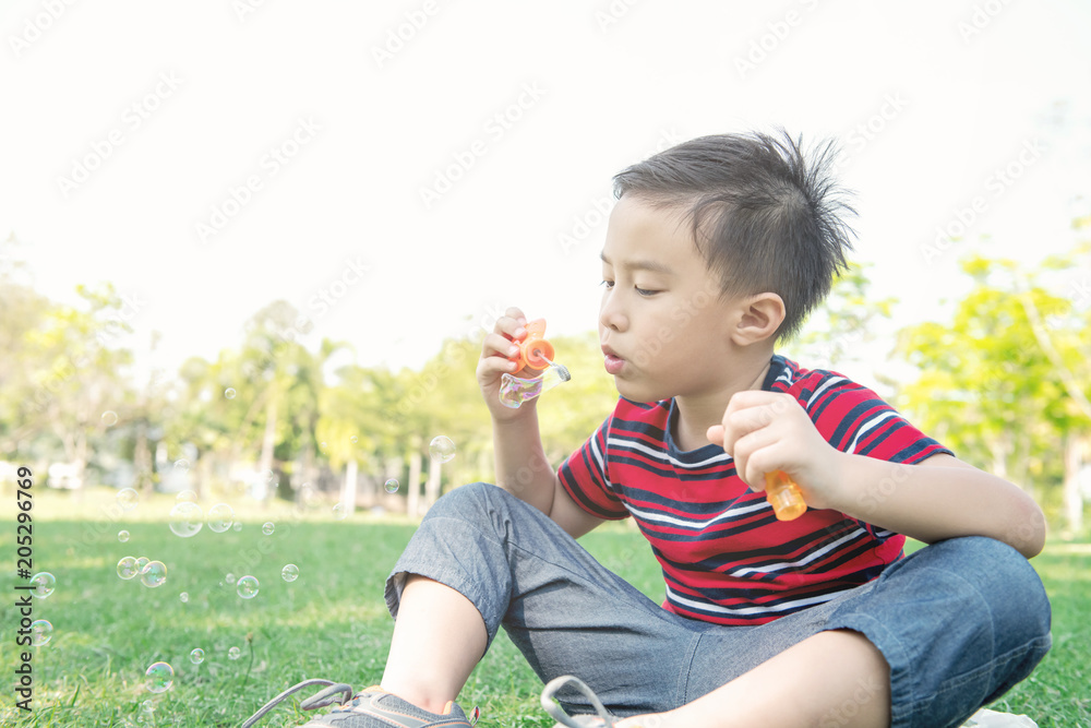 Young boy blowing bubble in park. Chinese boy enjoying playing with his bubble mixture in park. Young boy blowing bubble in park. Chinese boy enjoying playing with his bubble mixture in park.