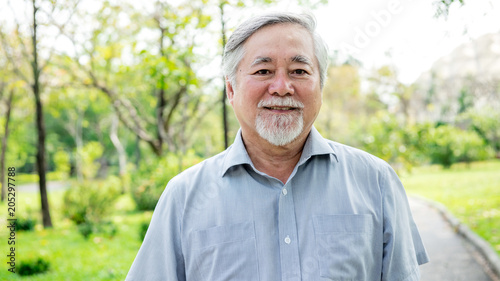 Portrait of senior man in park. Smiling chinese old man with park background. Medium shot.