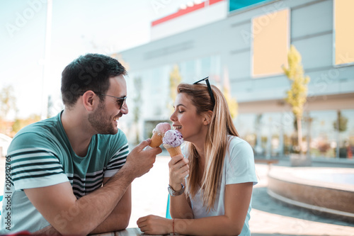 Happy young couple sitting in front of a mall and eating ice cream