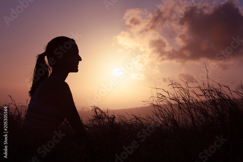 Young happy woman sitting outdoors watching the sunset. Enjoying life and nature concept.