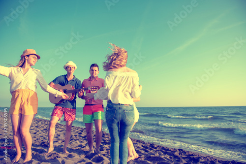 group of happy young people dancing at the beach on beautiful summer sunset