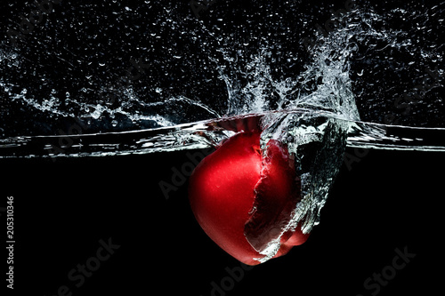 close up view of red apple falling into water isolated on black