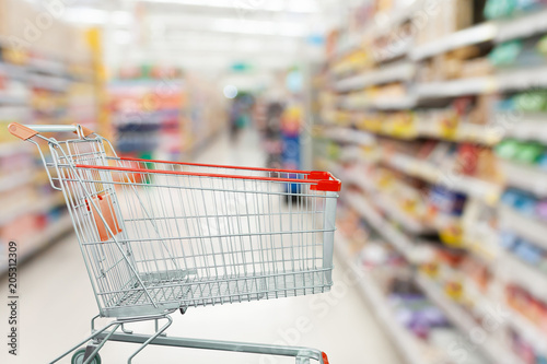 Supermarket aisle with empty shopping cart at grocery store retail business concept