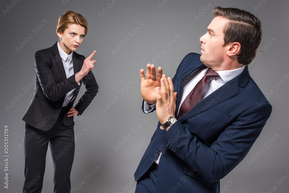 aggressive businesswoman quarreling and pointing at scared businessman, isolated on grey aggressive businesswoman quarreling and pointing at scared businessman, isolated on grey