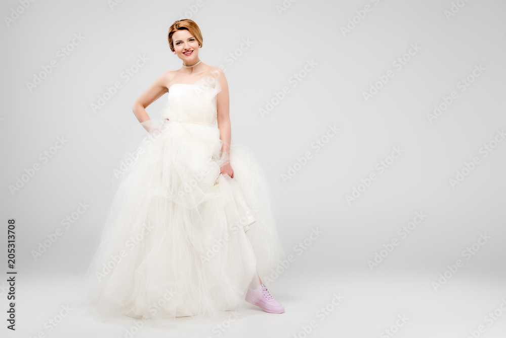 smiling bride in white wedding dress and pink sneakers, isolated on grey, feminism concept smiling bride in white wedding dress and pink sneakers, isolated on grey, feminism concept