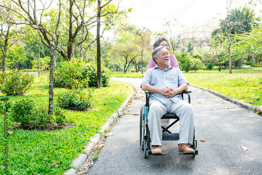 Senior couple in park and in wheelchair. Chinese old couple in park, relaxing, smiling. Man on wheelchair with his wife. Copy space. Senior couple in park and in wheelchair. Chinese old couple in park, relaxing, smiling. Man on wheelchair with his wife. Copy space.
