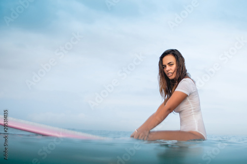side view of beautiful young woman in wet white swimsuit on surfboard in ocean
