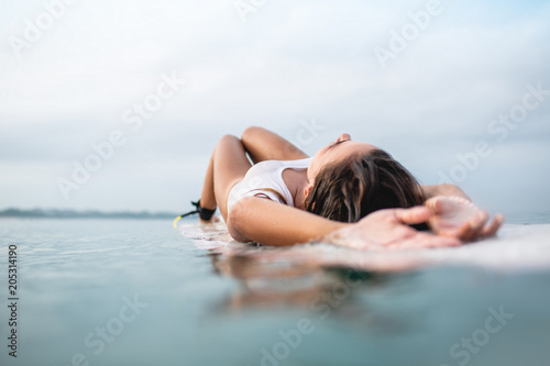 attractive young woman relaxing on surfboard in ocean