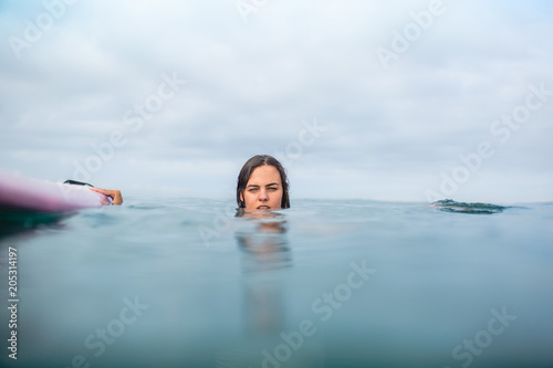 young woman swimming with surfboard on cloudy day