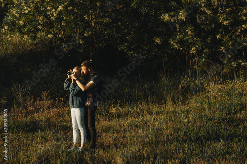 Full length portrait of amazing caucasian couple adventuring where man is teaching her girlfriend how to photograph landscapes against the sunlight. © Strelciuc