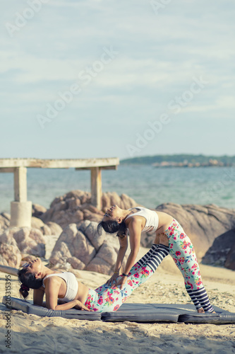 two asian woman playing yoga pose on sea beach