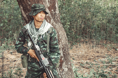 Soldier standing behind a tree ready to attack. Chinese male soldier standing behind a large tree looking around for his ememy.