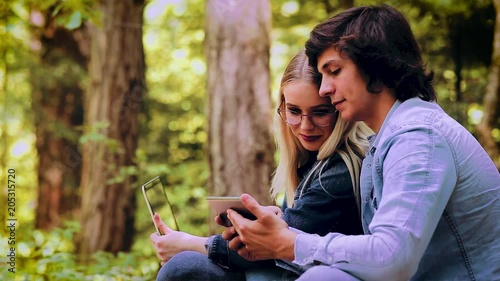 Young Couple Using Laptop And Tablet While Sitting In Forest photo