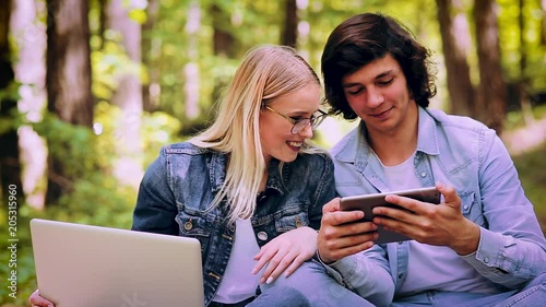 Young Couple Using Laptop And Tablet While Sitting In Forest photo