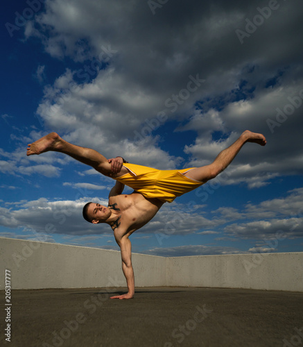 Tricking on street. Martial arts. Man kick with hand support barefoot. Shooted from bottom foreshortening against sky.