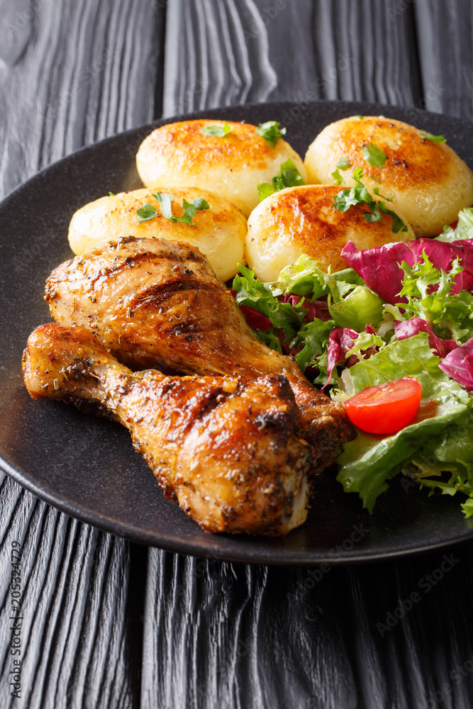 Delicious food: grilled chicken drumsticks with new potatoes and fresh salad closeup on a plate. vertical