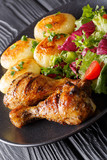 Grilled chicken drumsticks are served with potatoes and fresh salad close-up. vertical