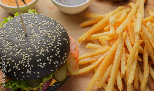 Black burger on a wooden background with potatoes and sauce photo