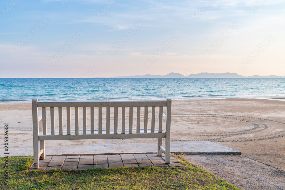 Fototapeta premium Relaksująca biała drewniana ławka przy nadbrzeżem z pięknym morzem i górą.