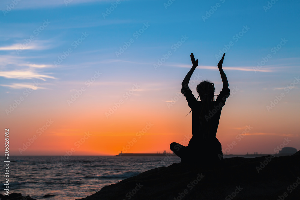 Yoga silhouette of woman meditating on the ocean beach during sunset.