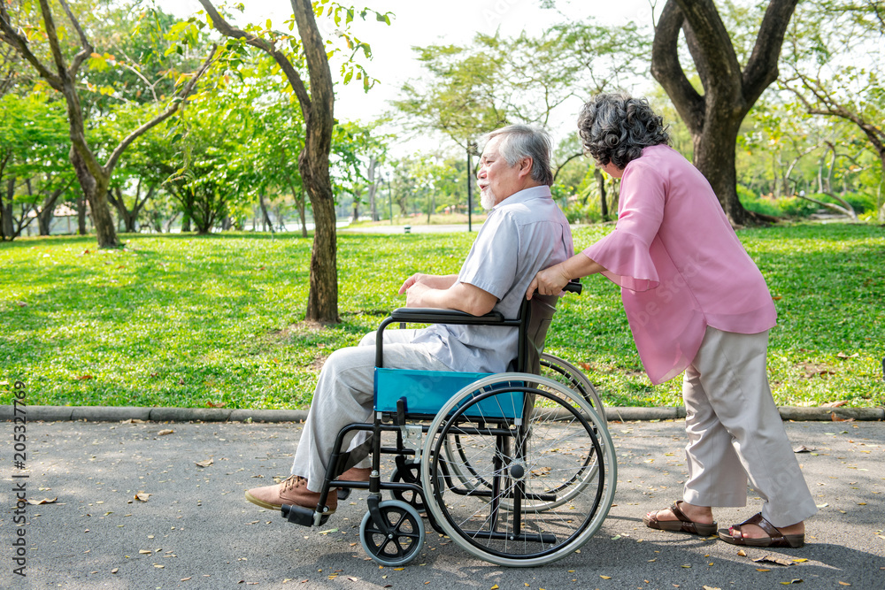 Senior couple in park and in wheelchair. Chinese old couple in park, relaxing, smiling. Man on wheelchair with his wife. Copy space. Senior couple in park and in wheelchair. Chinese old couple in park, relaxing, smiling. Man on wheelchair with his wife. Copy space.