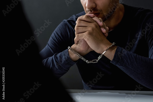 Criminal man with handcuffs in interrogation room