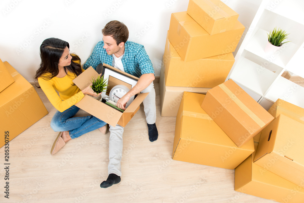 Couple sitting on the floor unpacking box after moving into new house Couple sitting on the floor unpacking box after moving into new house