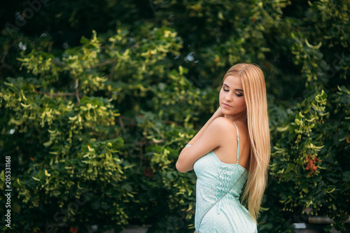 Blonde girl in turquoise color dress posing to the photographer