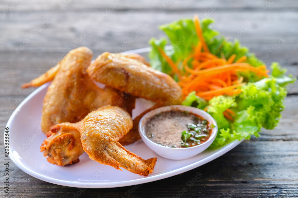Fried chicken in a white dish with vegetables and dipping sauce on a wooden table.