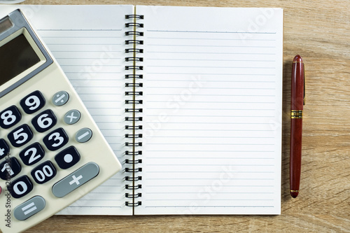 Fountain pen or ink pen with notebook paper and calculator on wooden working table with copy space, office desk concept. top view..