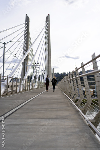 Two girls with backpacks walking through Tilikum Crossing Bridge across the Willamette River in Portland Oregon © vit