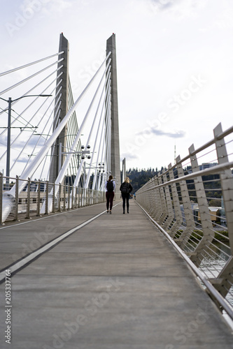 Two girls with backpacks walking through Tilikum Crossing Bridge across the Willamette River in Portland Oregon