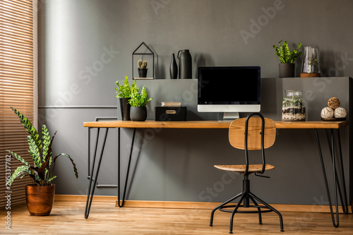 Canvas Print Simple workspace interior with wooden chair at the desk standing against black wall in a room with plants