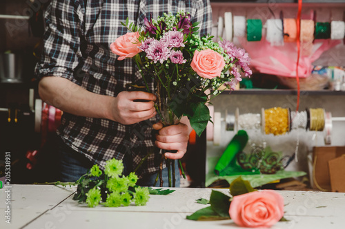 Florist man collects a modern bouquet of pink roses, hibiscus.
