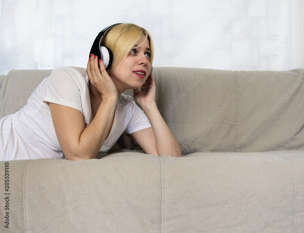 Pretty young woman in headphones lying on sofa listening music or audio book with closed eyes. Joyful beautiful lady enjoying popular songs, relaxing on coach at home. Female music lover portrait Pretty young woman in headphones lying on sofa listening music or audio book with closed eyes. Joyful beautiful lady enjoying popular songs, relaxing on coach at home. Female music lover portrait