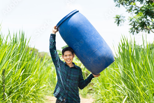 Young Asian farmer carry blue water tank (fermented water tank) for watering in Napier grass field
