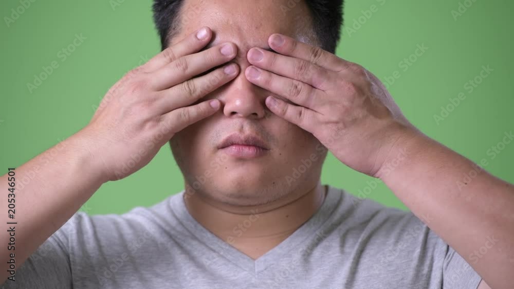 Young handsome overweight Asian man against green background Young handsome overweight Asian man against green background