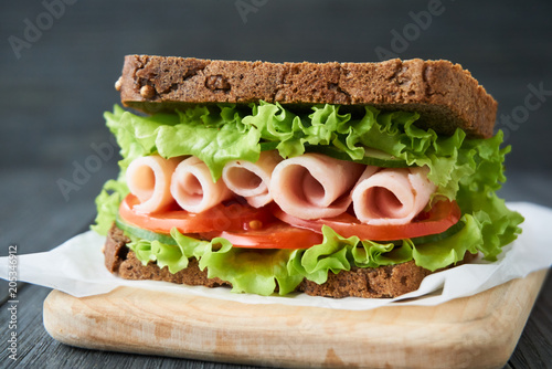 Sandwich with ham, tomato, cucumber and lettuce on a wooden cutting board