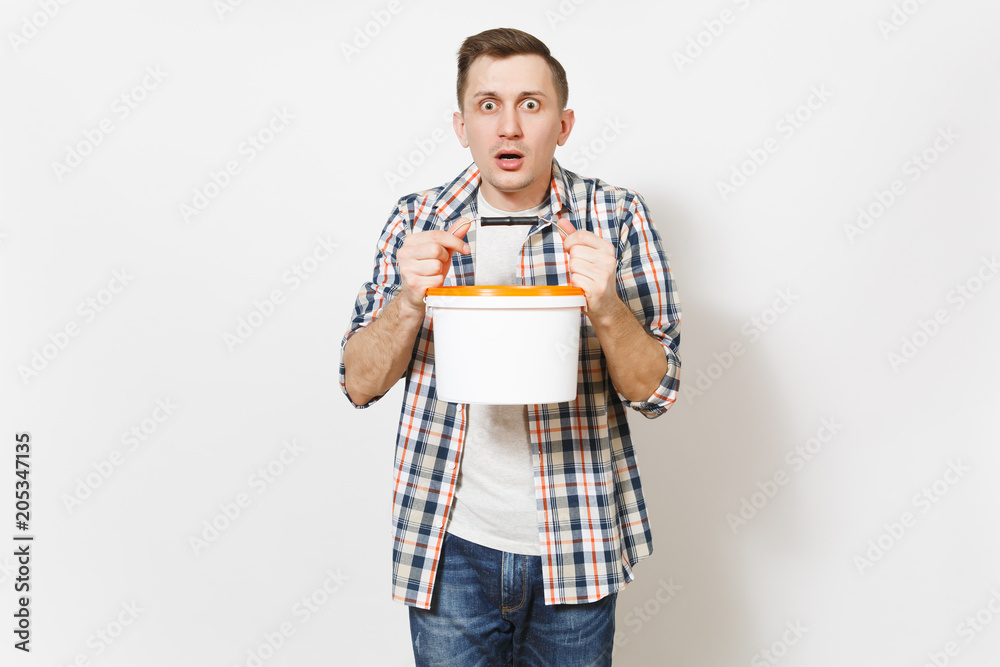 Young shocked handsome man in casual clothes holding empty paint bucket with copy space isolated on white background. Instruments, accessories for renovation apartment room. Repair home concept. Young shocked handsome man in casual clothes holding empty paint bucket with copy space isolated on white background. Instruments, accessories for renovation apartment room. Repair home concept.