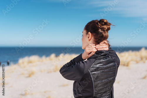 Woman walking on a beach rubbing her neck