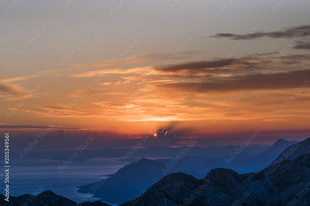  Sunset panorama in Biokovo Nature Park with interesting luminous clouds, the Dalmatian coast of the Adriatic Sea and mountain ranges in shades of blue - View from Sveti Jure, Croatia
