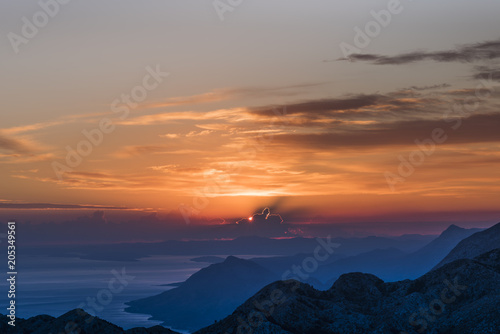  Sunset panorama in Biokovo Nature Park with interesting luminous clouds, the Dalmatian coast of the Adriatic Sea and mountain ranges in shades of blue - View from Sveti Jure, Croatia