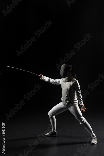 full length of female fencer in uniform posing with sword on black background