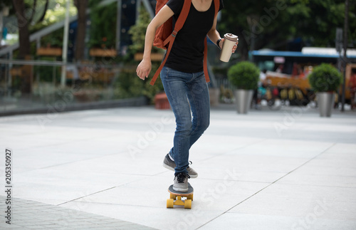 woman skateboarding with coffee cup in hand on city street