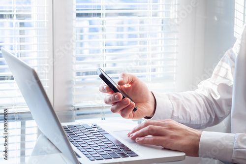 Businessman working with laptop and smartphone, bright office, financial accountant photo