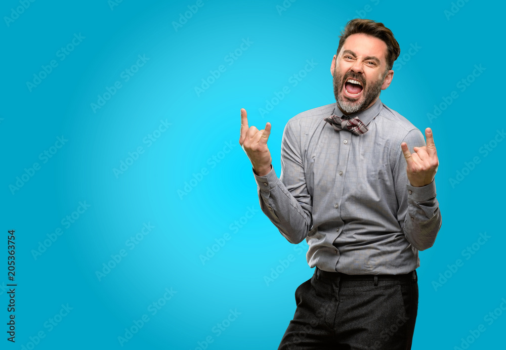 Middle age man, with beard and bow tie making rock symbol with hands, shouting and celebrating Middle age man, with beard and bow tie making rock symbol with hands, shouting and celebrating