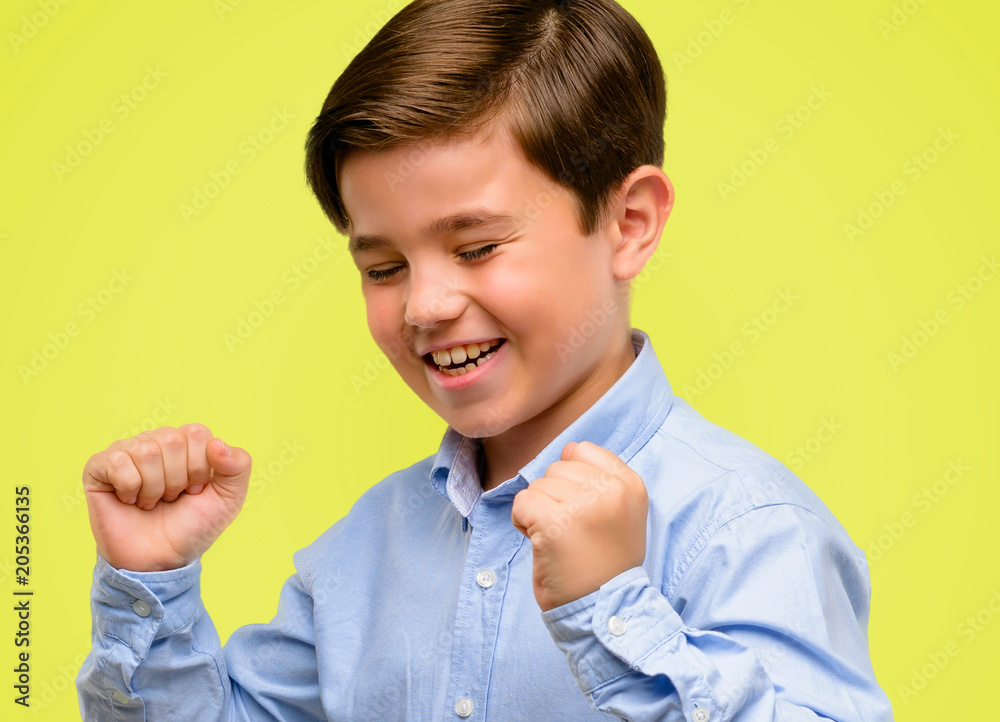 Handsome toddler child with green eyes happy and surprised cheering expressing wow gesture over yellow background Handsome toddler child with green eyes happy and surprised cheering expressing wow gesture over yellow background
