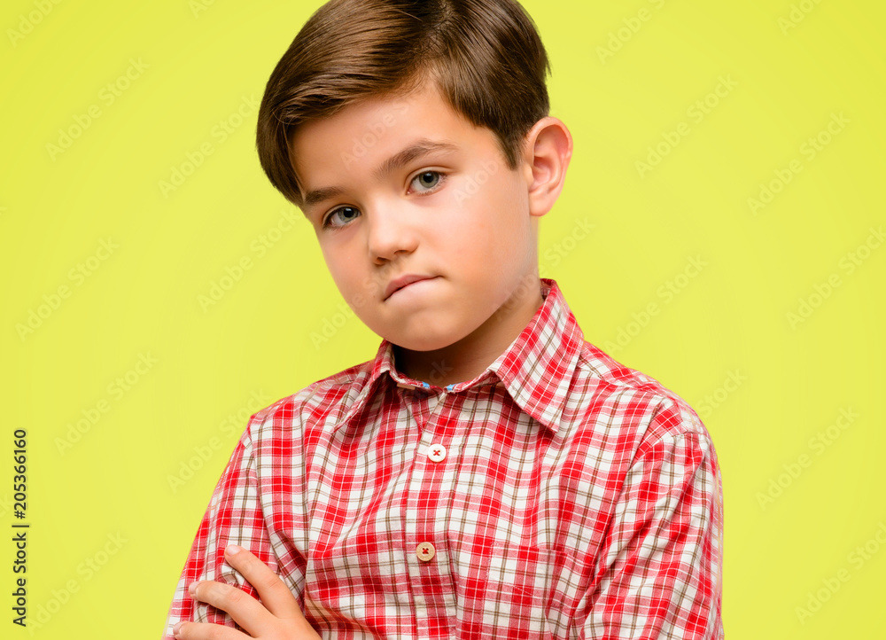 Handsome toddler child with green eyes nervous and scared biting lips looking camera with impatient expression, pensive over yellow background Handsome toddler child with green eyes nervous and scared biting lips looking camera with impatient expression, pensive over yellow background